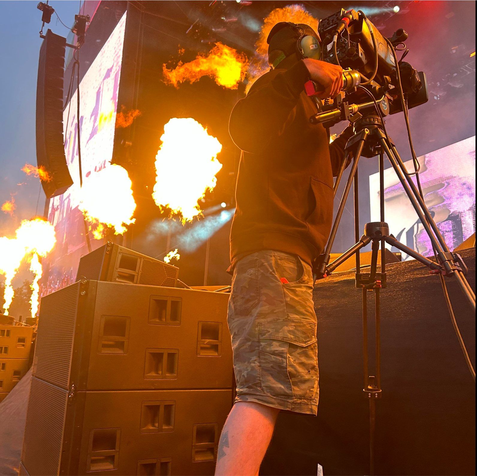 Daniel running a broadcast camera on stage as pyro fires behind him at a Metallica stadium show